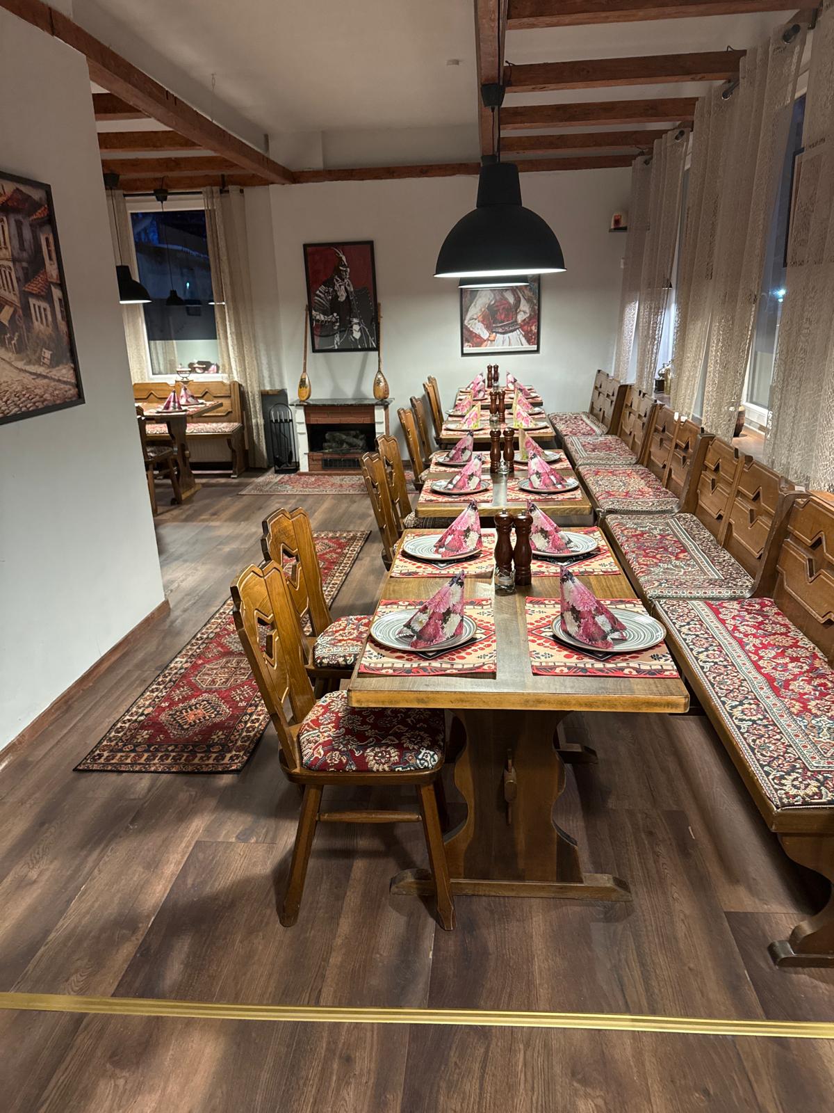 Der Gastraum des Troja Restaurants mit langen Holztischen und traditionellen Teppichen